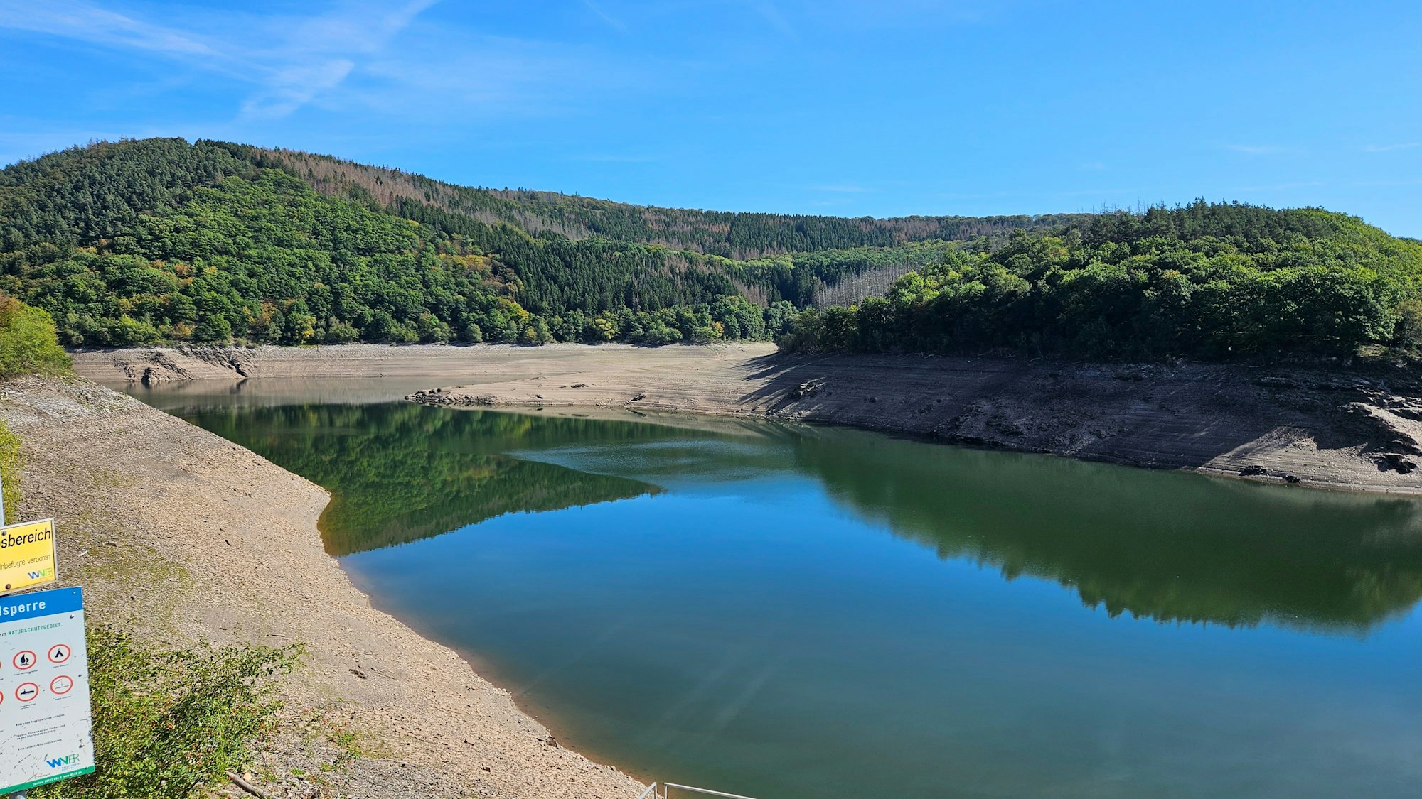 Der niedrige Wasserstand im Urftsee mit braunen Rändern an den Ufern ist zu sehen.