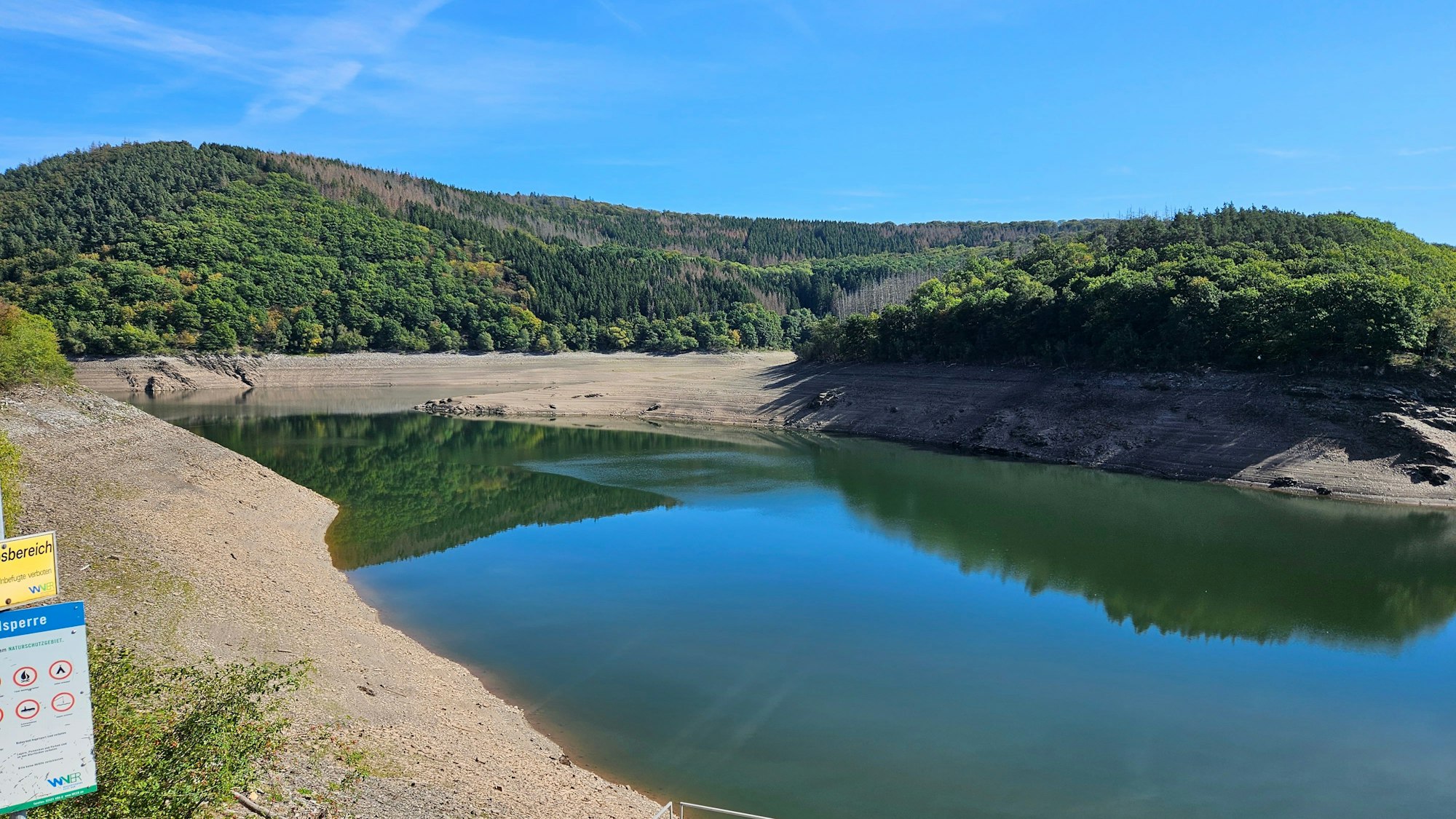 Der niedrige Wasserstand im Urftsee mit braunen Rändern an den Ufern ist zu sehen.