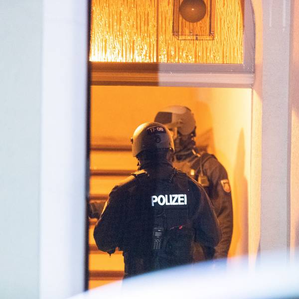 Zwei Polizisten stehen hinter einer Haustür im Treppenhaus.