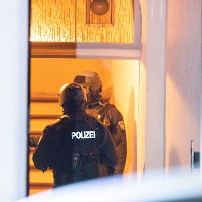 Zwei Polizisten stehen hinter einer Haustür im Treppenhaus.