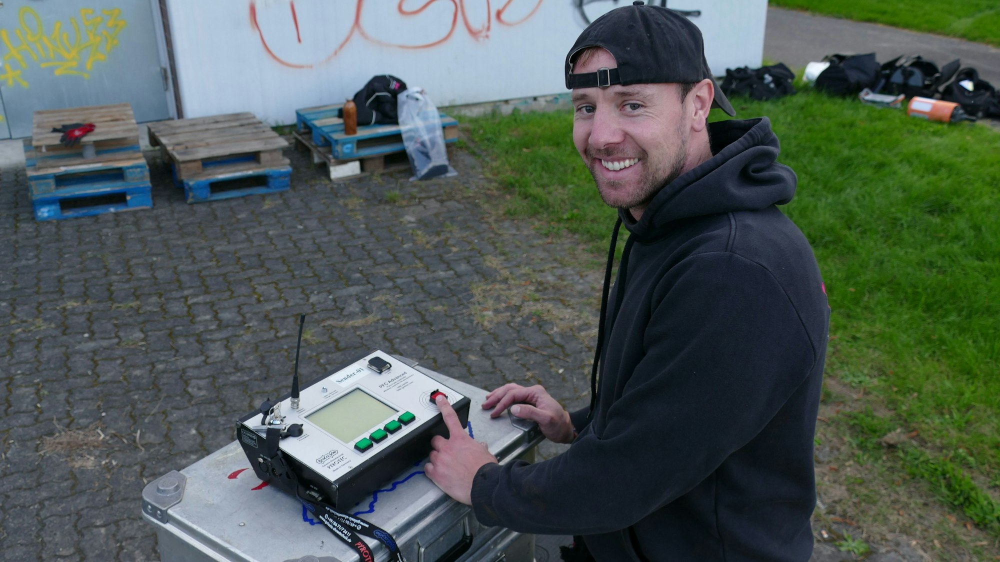 Ein Mann im schwarzen Hoodie und mit schwarzer Base-Cap steht an einem Schaltpult.