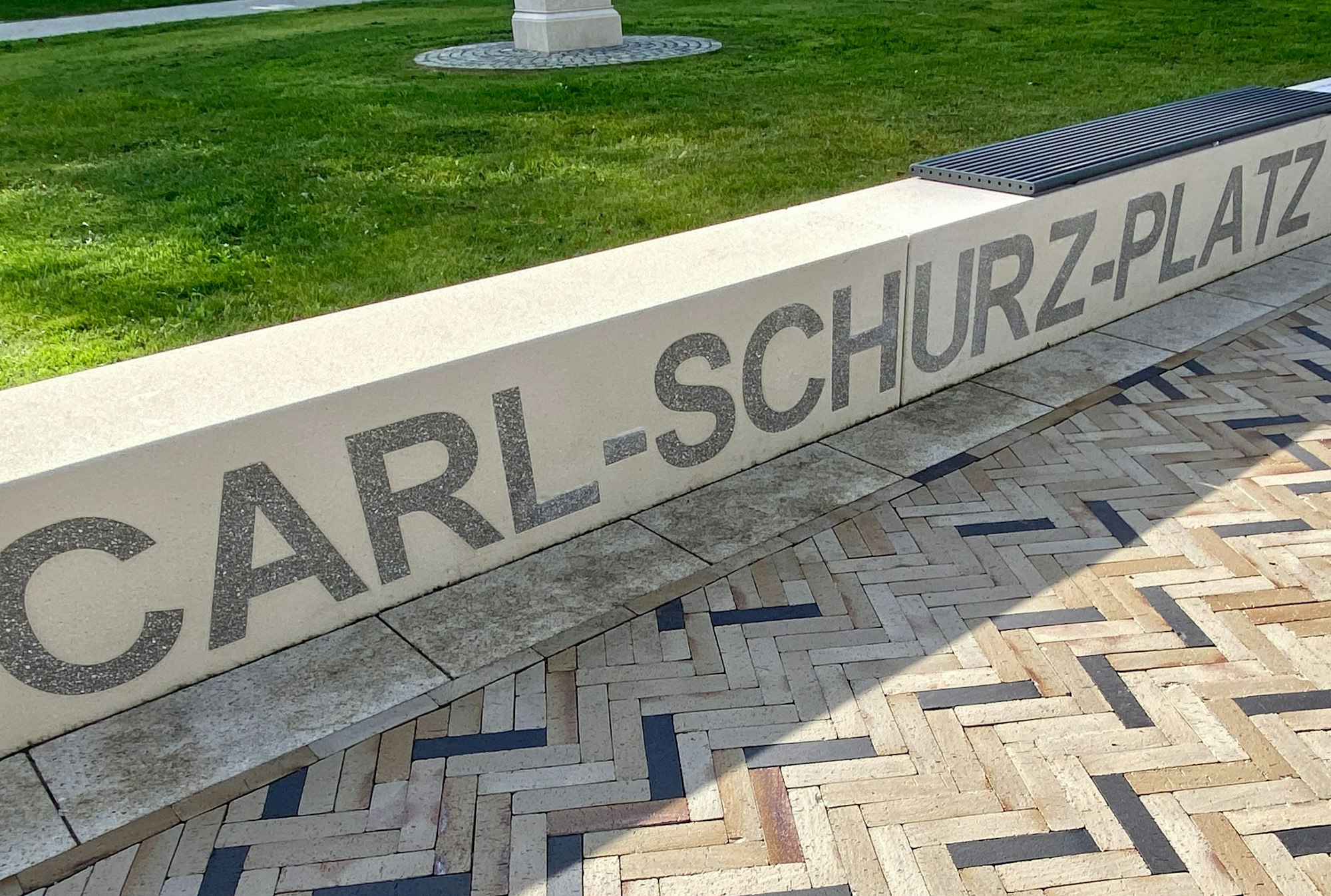 Der großformatige Schriftzug "Carl-Schurz-Platz" ist auf einer steinernen Sitzbank zu lesen.