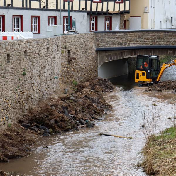 Ein Bagger steht in der Erft in Bad Münstereifel. Zu sehen sind auch die wieder aufgebauten Erftmauern.