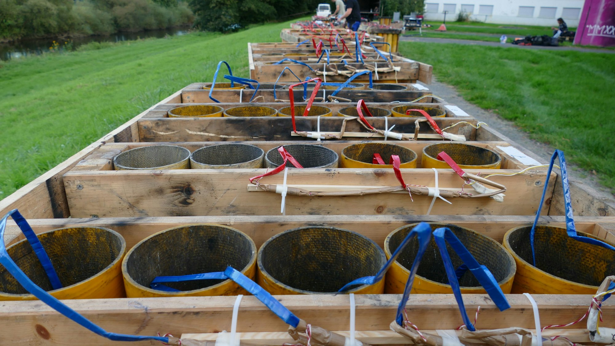 Auf einer Wiese stehen in Holzvorrichtungen Papprohre, aus denen Zündschnüre kommen.