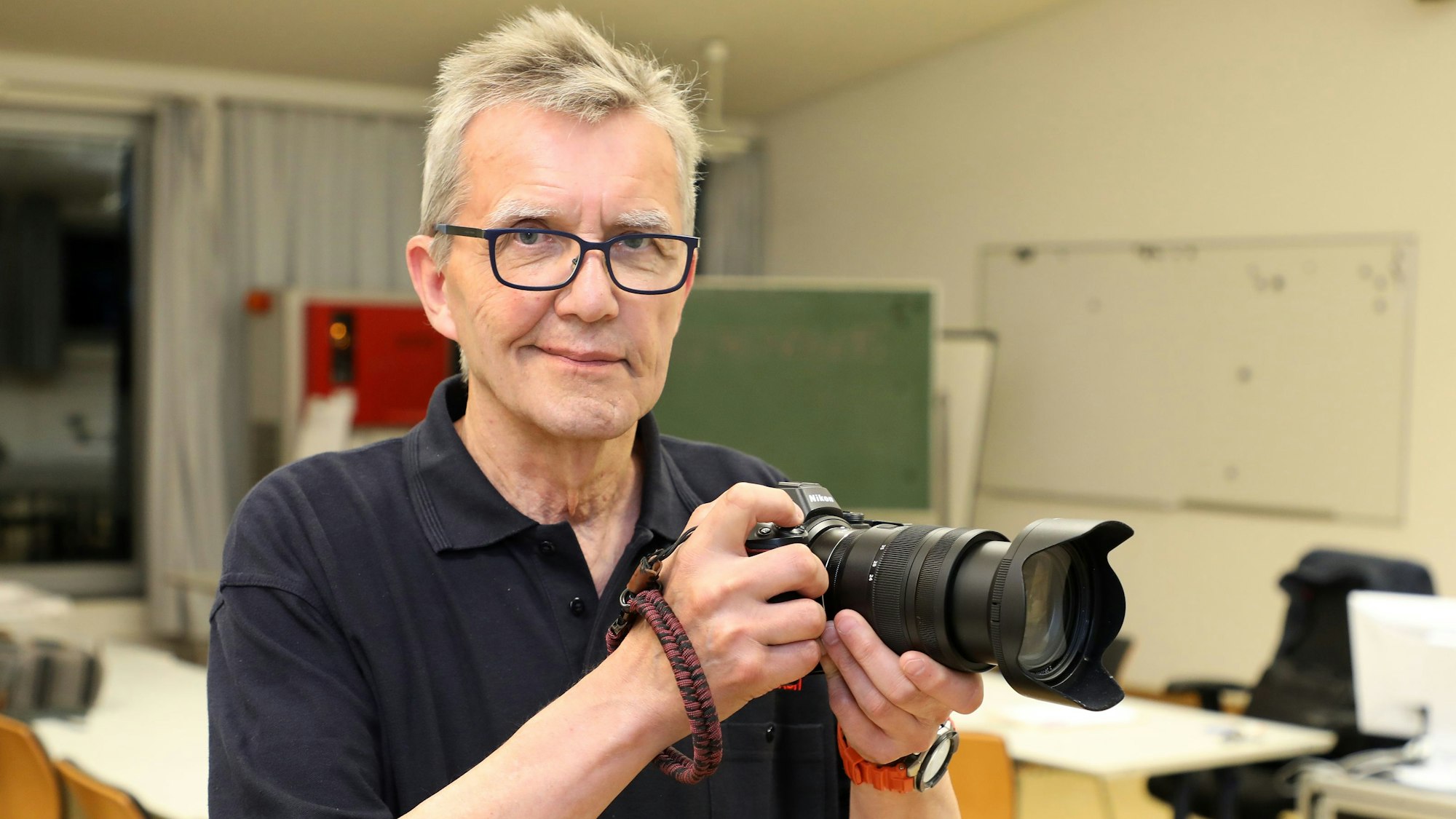 Ein Mann mit Kamera steht in einem Raum und schaut in die Kamera des Fotografen.