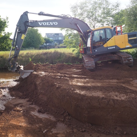 Ein Bagger schaufelt Erde weg, sodass Wasser in eine Rinne fließt.