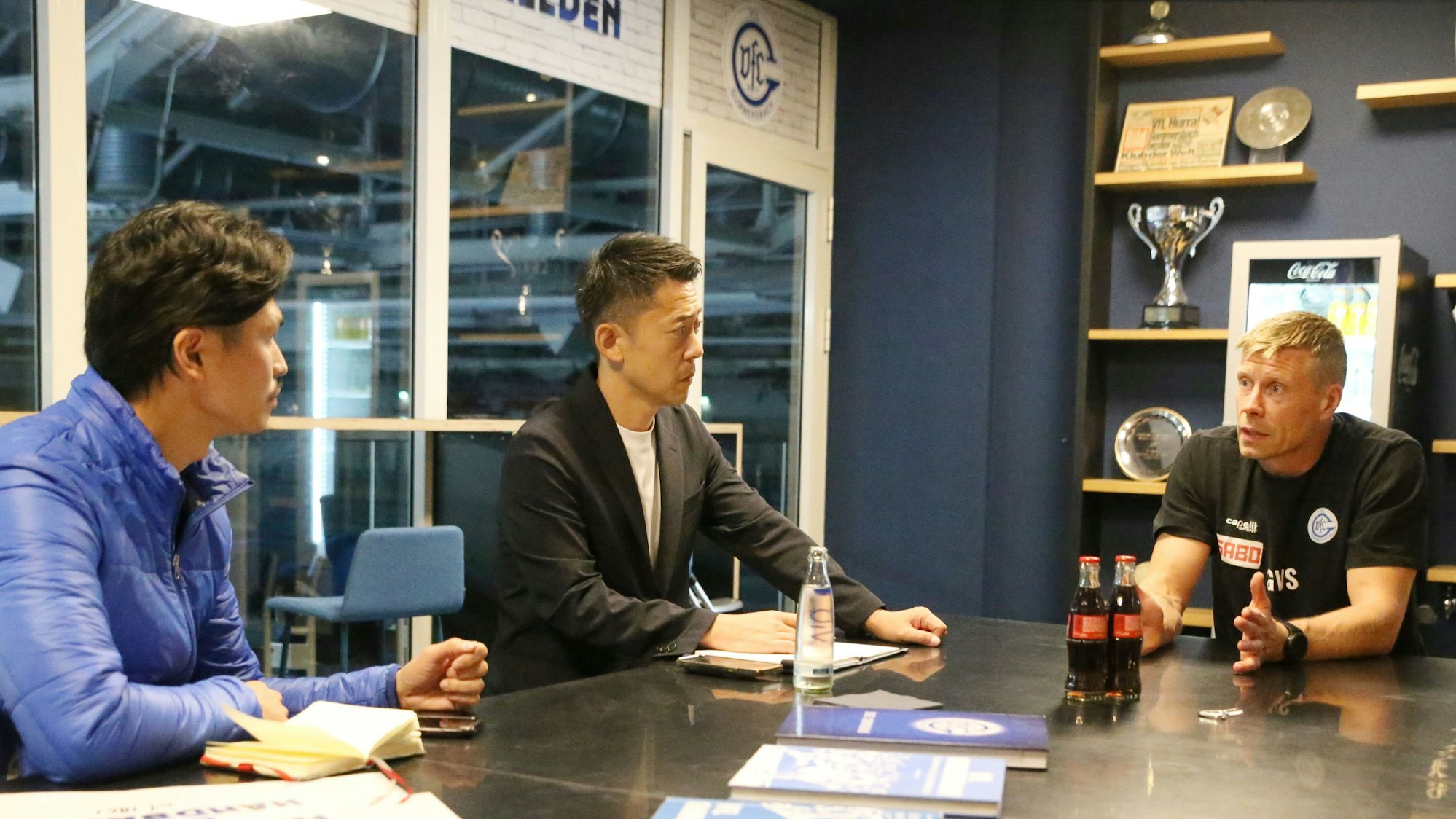 Am Tisch sitzen VfL-Trainer Gudjon-Valur Sigurdsson mit Ayumu Muta und Akyama Shigeki.