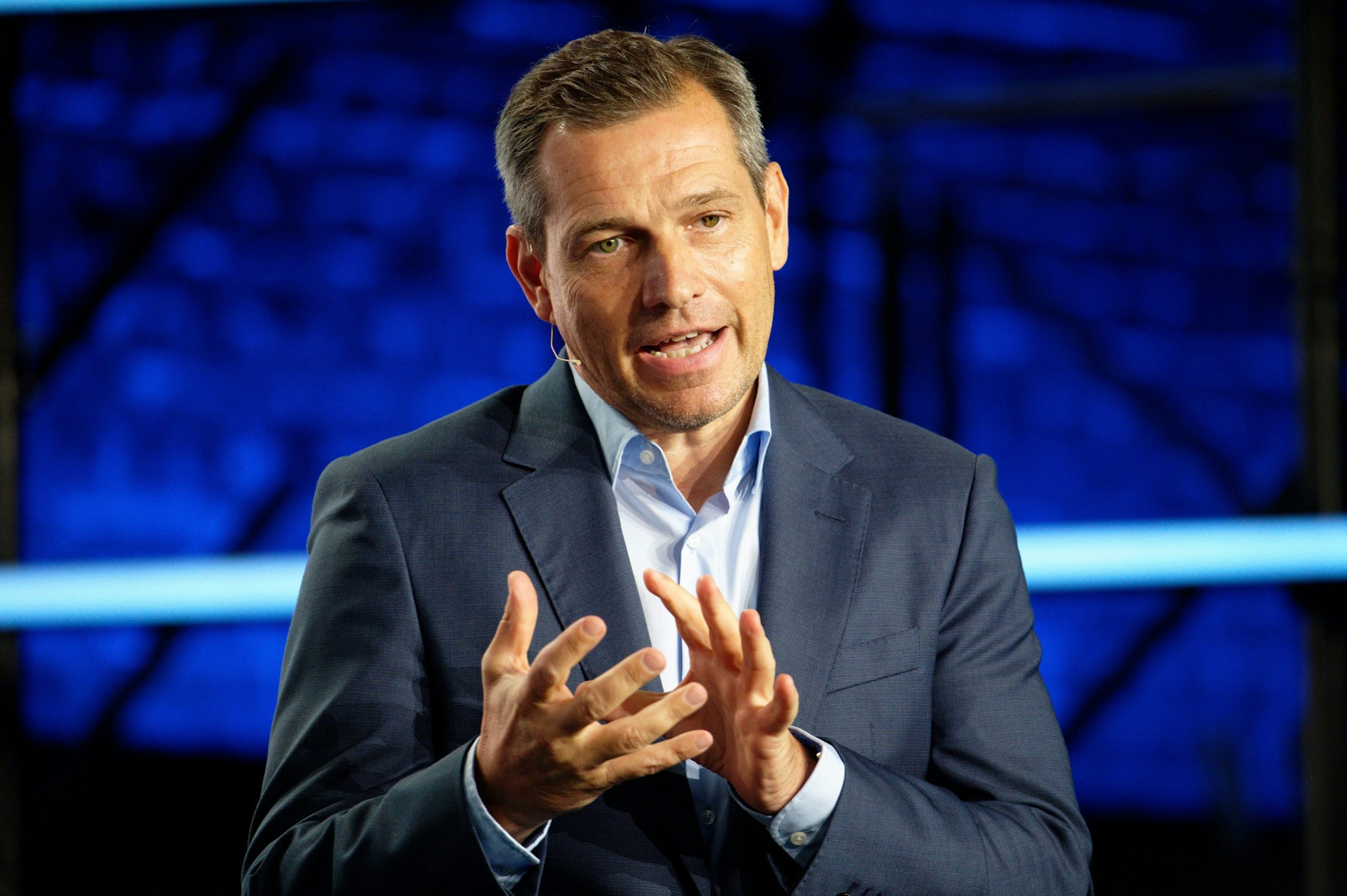 Der Eventmanager Michael Mronz steht auf einer blau beleuchteten Bühne und spricht zu einem nicht sichtbaren Publikum.