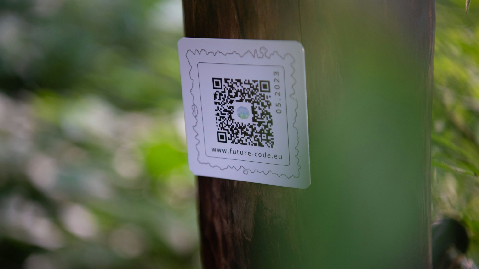 Ein kleines weißes Schild ist an einem Zaunpfahl angebracht, darauf ist ein QR-Code gedruckt.