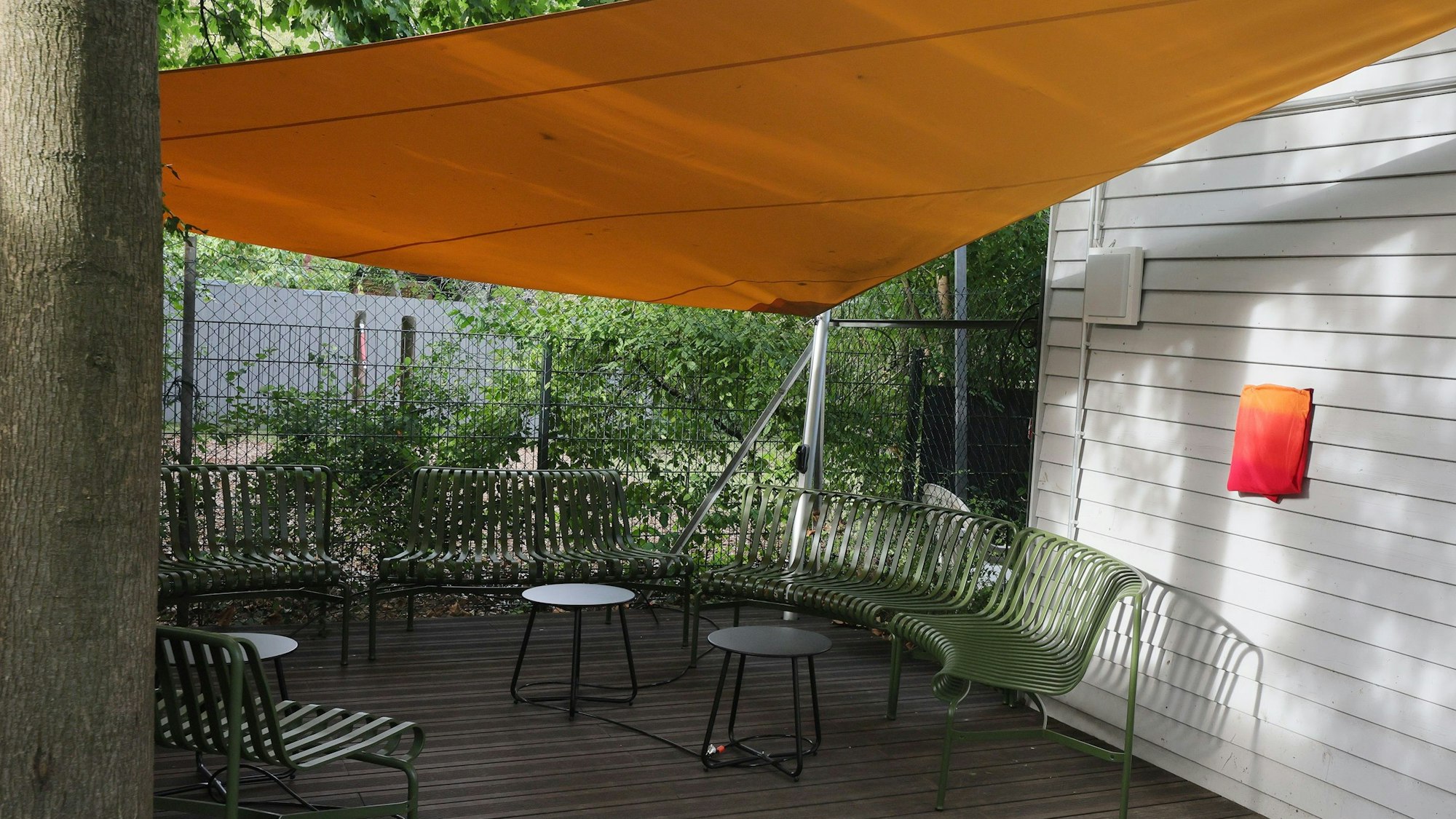 Terrasse mit Stühlen, Tischen und einem gelben Segel, das darüber gespannt ist