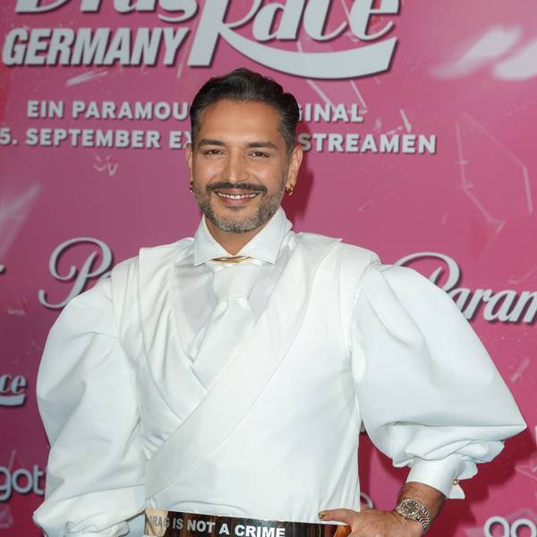 Gianni Jovanovic bei der Premiere der Show „Drag Race Germany“, die beim Streamingdienst Paramount+ zu sehen ist. Er trägt ein weißes Hemd, eine weiße Krawatte und lächelt in die Kamera.
