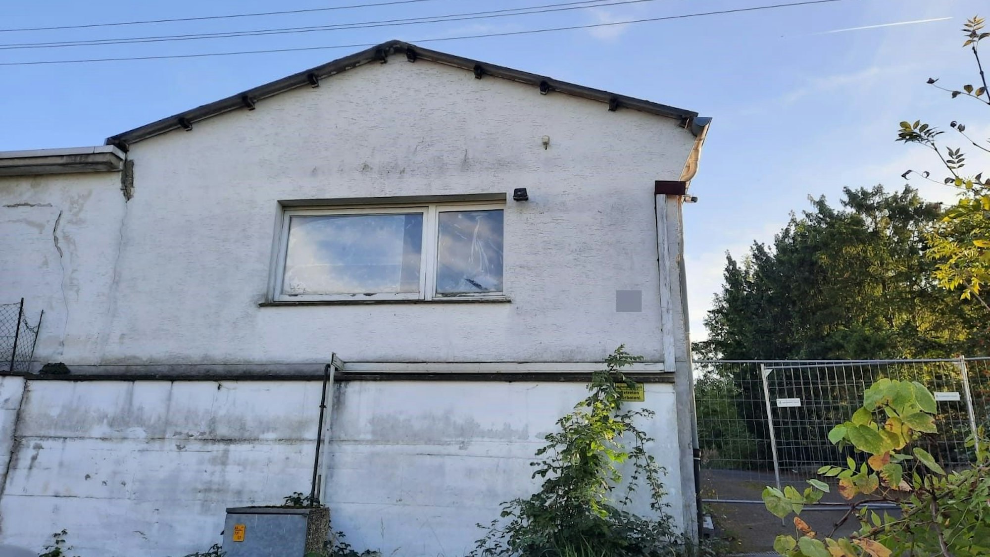 Eine alte Gewerbehalle; ein Bauzaun versperrt den Zugang zum Gebäude.