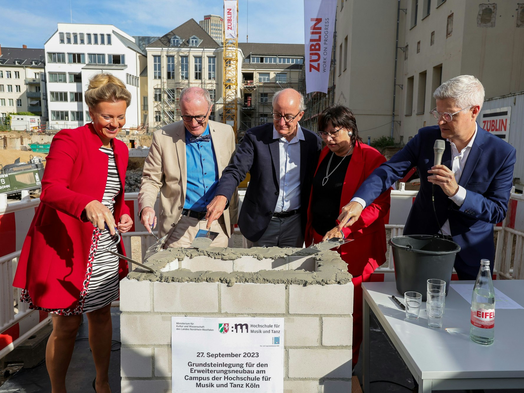 Zwei Frauen und drei Männer verteilen Mörtel auf einem gemauerten Rechteck.