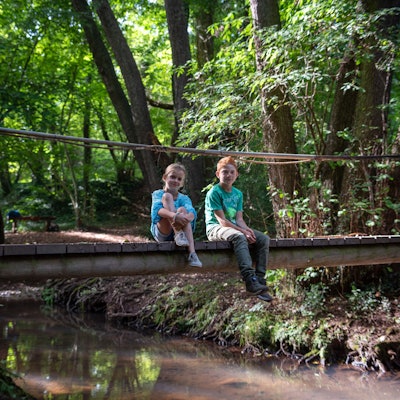 Ein Mädchen und ein Junge sitzen auf einer kleinen Brücke mitten im Wald.