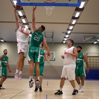 Basketballspielszene unter dem Korb: Ein Zülpicher Spieler steigt zum Sprungwurf hoch, ein Aachener Spieler blockt ihn.