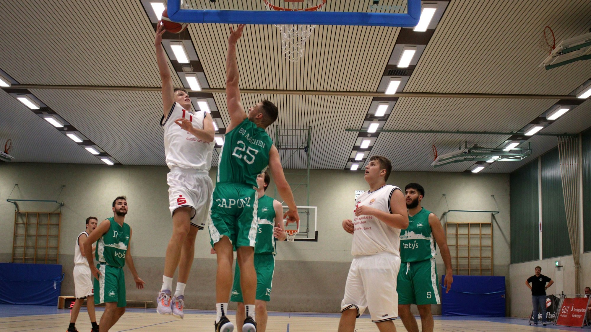 Basketballspielszene unter dem Korb: Ein Zülpicher Spieler steigt zum Sprungwurf hoch, ein Aachener Spieler blockt ihn.