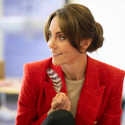 Die Prinzessin von Wales hält eine Feder in der Hand und blickt zur Seite.