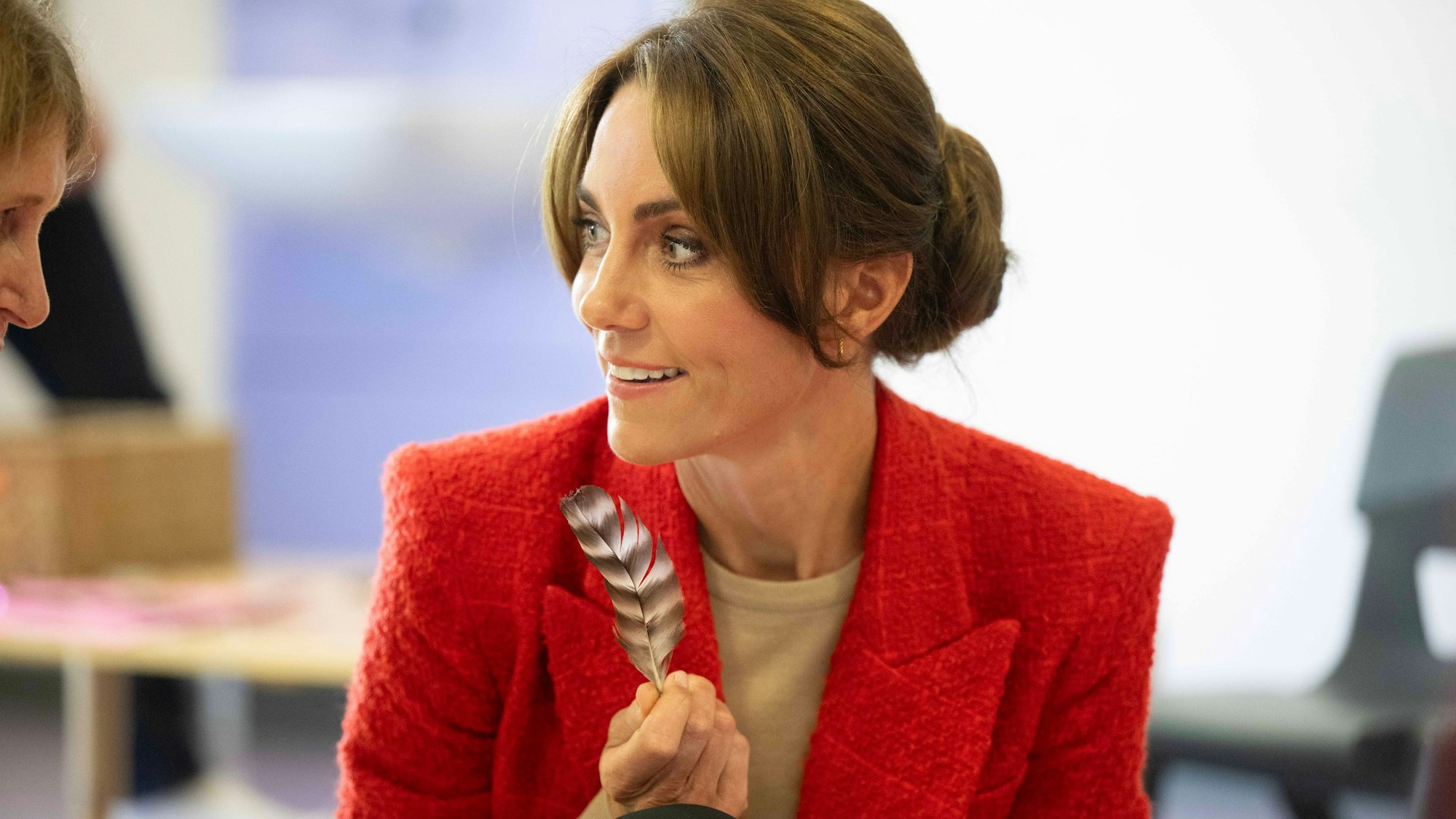 Die Prinzessin von Wales hält eine Feder in der Hand und blickt zur Seite.