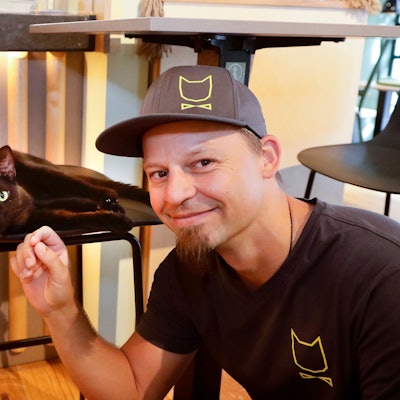 Michael Guddat, Tierpsychologe, Katzensitter und Katzenexperte, mit einer schwarzen Katze im Café Katzentempel in der Kölner Severinstrasse.