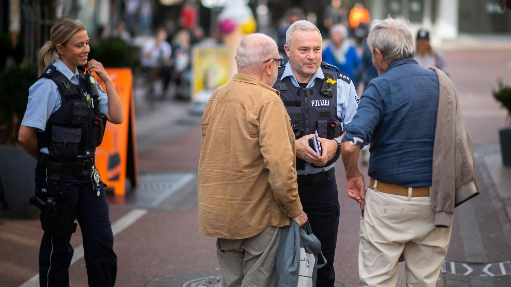 Das Bild zeigt den Bezirksbeamten Ralf Zenner in Polizeiuniform im Gespräch mit zwei Passanten.
