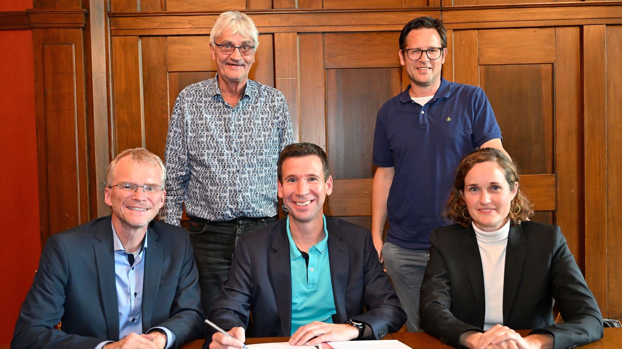 Am Tisch sitzen Bürgermeister Stein, Christian Metten und Jennifer Vollmer. Der Vertrag liegt vor ihnen. Hinter ihnen stehen Marco Häusling und Ron Woydowski.