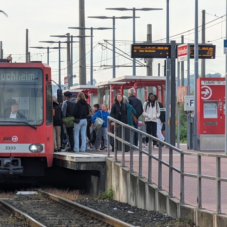 Eine Straßenbahn steht am bevölkerten Bahnsteig in Hermülheim.