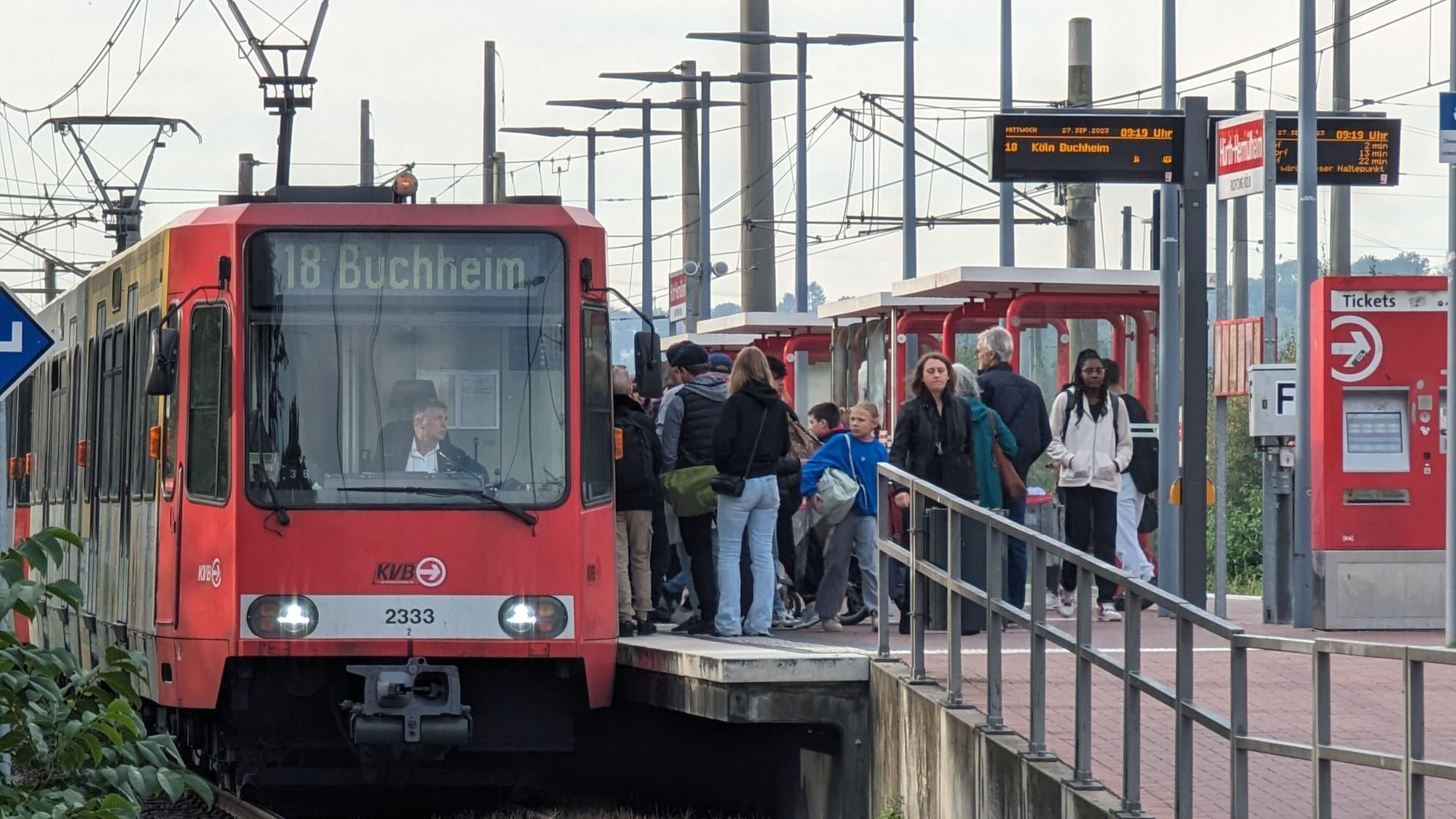 Eine Straßenbahn steht am bevölkerten Bahnsteig in Hermülheim.