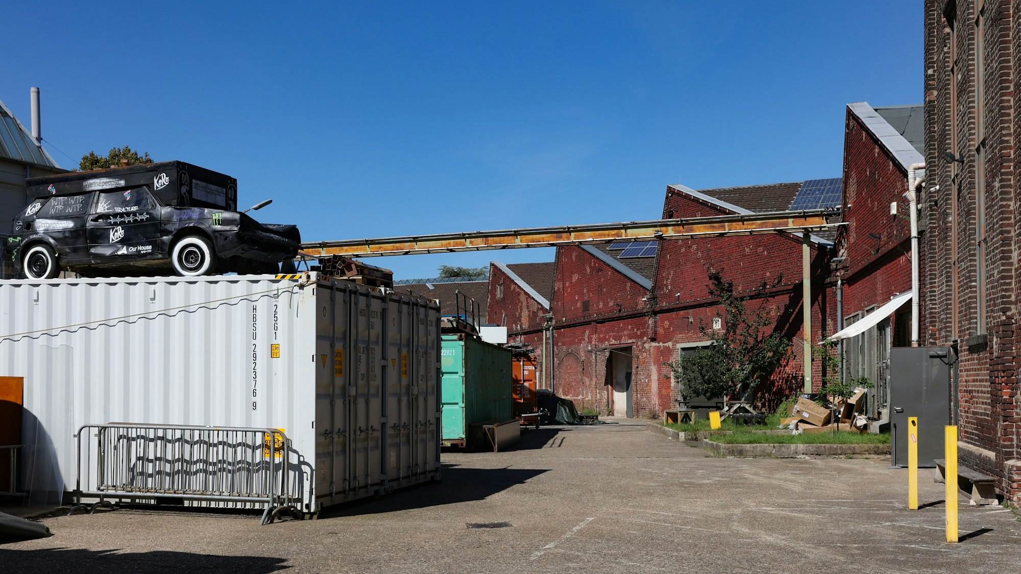 Das Gelände der Hallen Kalk: Auf demBild sind mehrere Gebäudeteile und ein Container mit einem Auto auf dem Dach zu sehen.