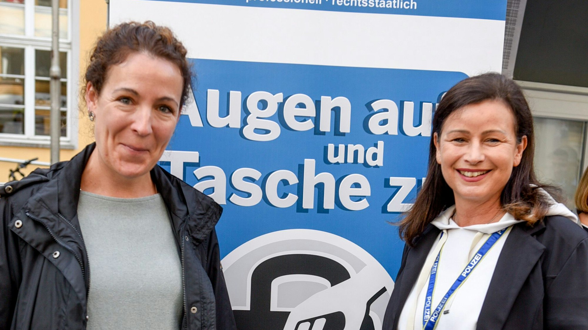 Das Bild zeigt die Polizistinnen Rebecca Schmitz und Martina Rautenberg vor einem Plakat.