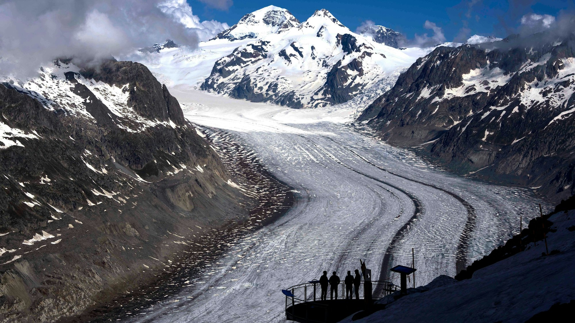 ARCHIV - 14.06.2023, Schweiz, Goms: Menschen genießen die Aussicht auf den Aletschgletscher in der Nähe von Goms. Die Schweizer Gletscher haben nach 2022 ein zweites Extremjahr erlebt. In beiden Jahren zusammen ist das Gletschervolumen um zehn Prozent geschrumpft, wie die Schweizerische Kommission für Kryosphärenbeobachtung der Akademie der Naturwissenschaften am Donnerstag berichtete. (zu dpa: «Zweites Extremjahr für Schweizer Gletscher») Foto: Matthias Schrader/AP +++ dpa-Bildfunk +++