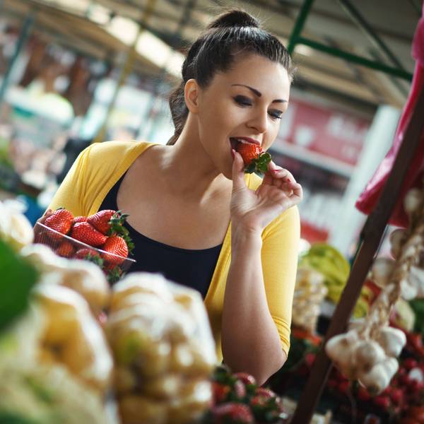 Frau probiert eine Erdbeere im Supermarkt.