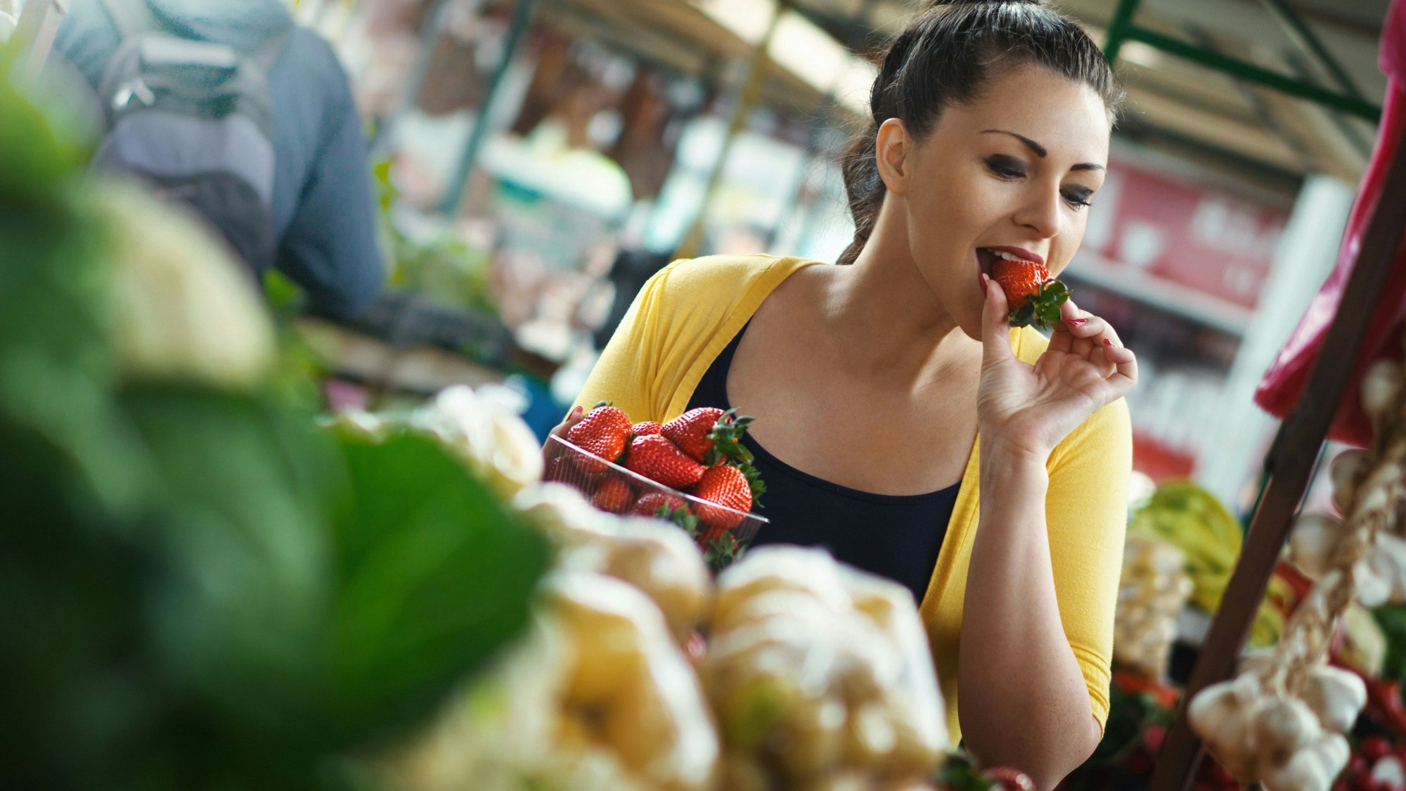 Frau probiert eine Erdbeere im Supermarkt.
