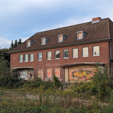 Ein altes, zugewuchertes Bahnhofsgebäude mit vernagelten Türen und Fenstern.