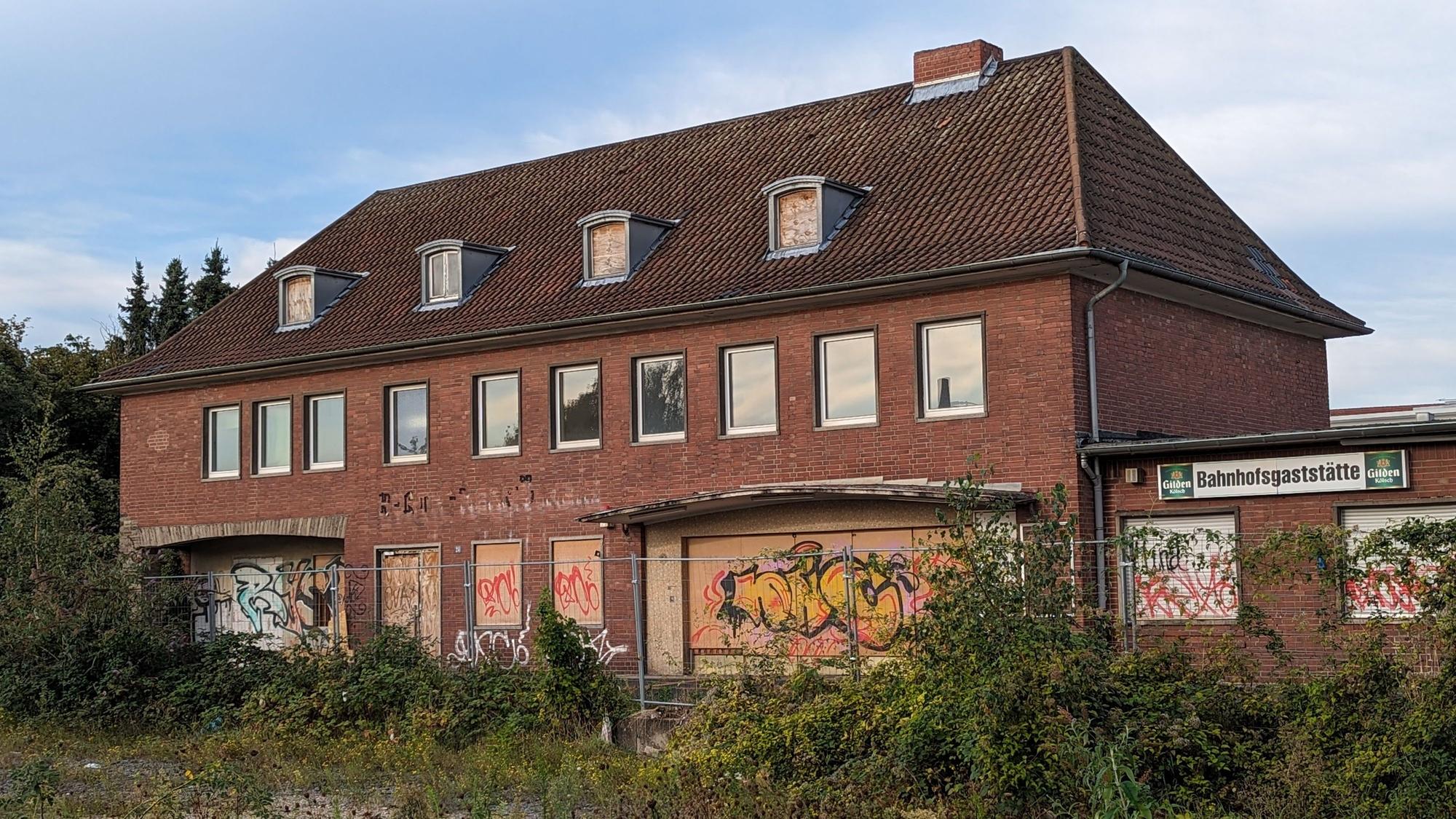 Ein altes, zugewuchertes Bahnhofsgebäude mit vernagelten Türen und Fenstern.
