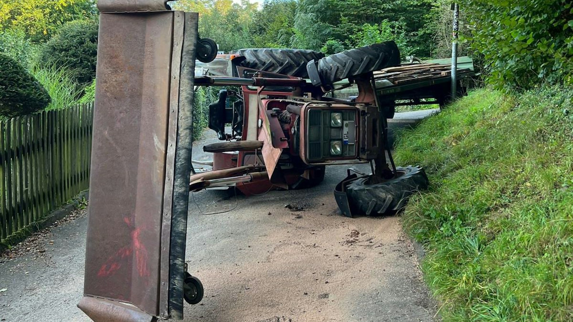 Ein Traktor liegt auf der Seite, dahinter steht ein Anhänger.