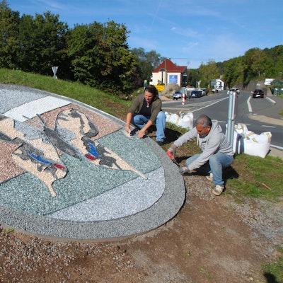 Auf der Insel des Kreisverkehrs in Ahrhütte legen ein Mann und eine Frau ein Schmetterlings-Bild aus farbigem Splitt.