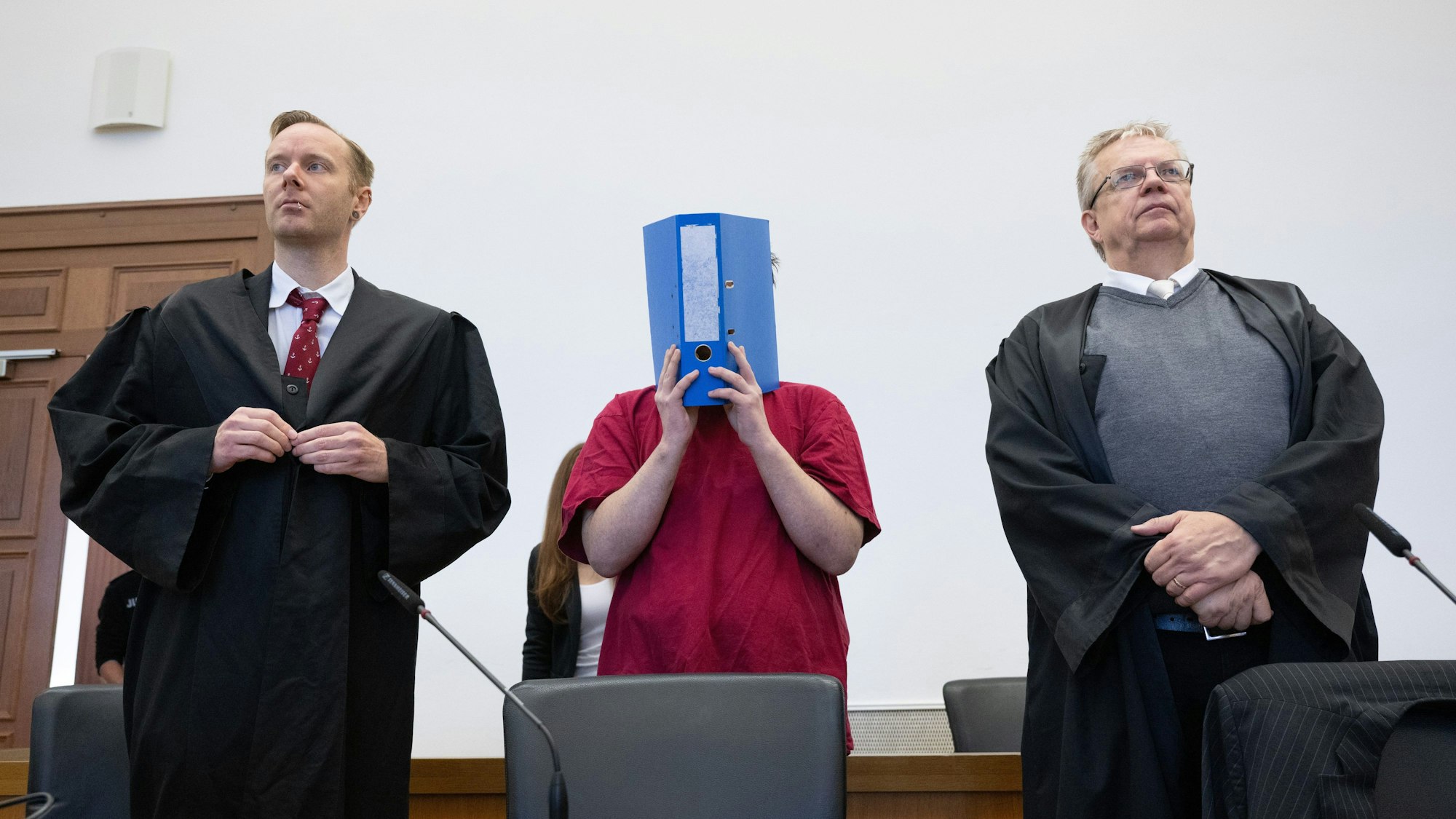 Der Angeklagte verbirgt sein Gesicht hinter einem Aktenordner.