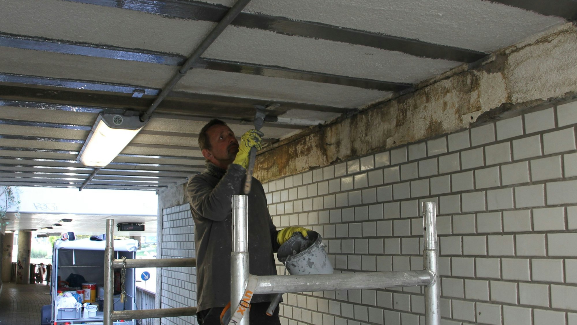 Ein Maler auf einem Gerüst streicht die Decke der Unterführung an der Mahrstraße