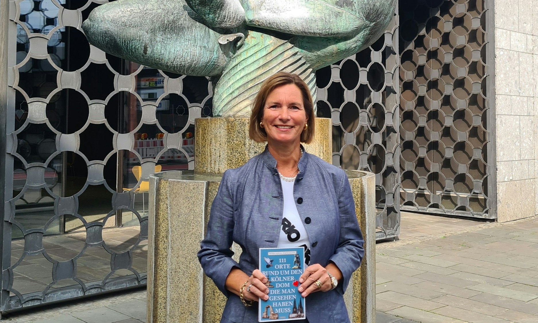 Autorin Petra Sophia Zimmermann präsentiert ihr neues Buch vor dem Baptisterium am Kölner Dom.