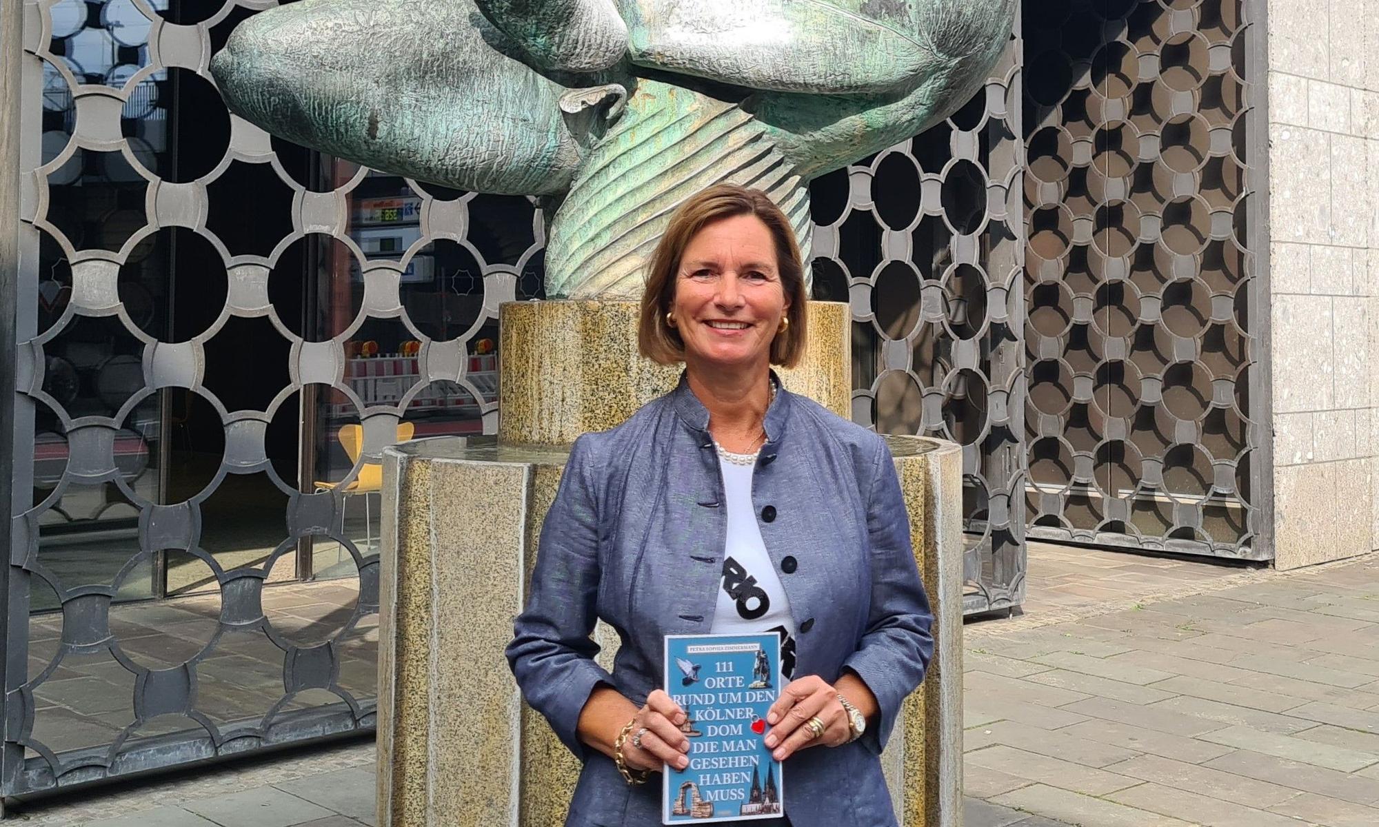 Autorin Petra Sophia Zimmermann präsentiert ihr neues Buch vor dem Baptisterium am Kölner Dom.