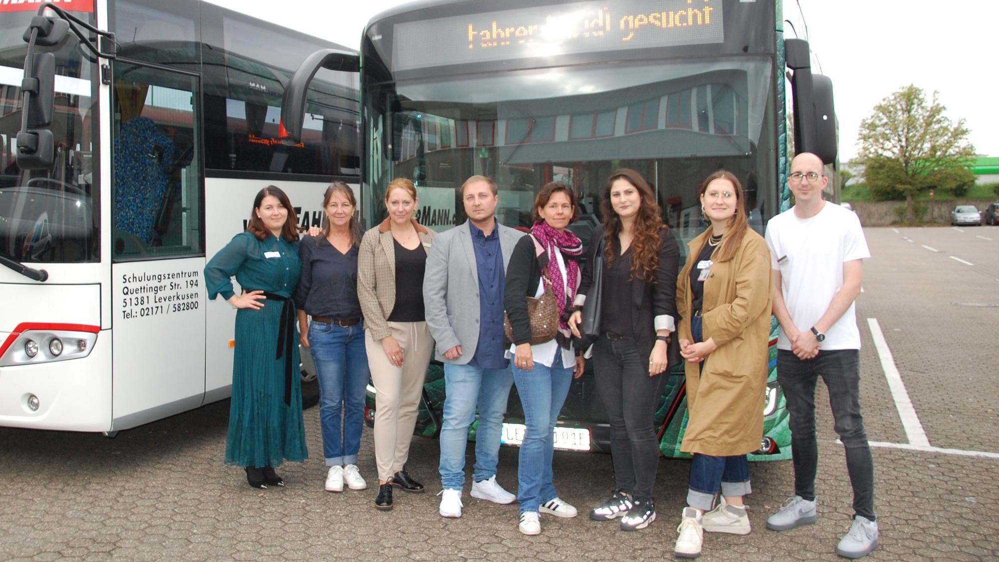 Sechs Frauen und zwei Männer stehen vor Bussen.