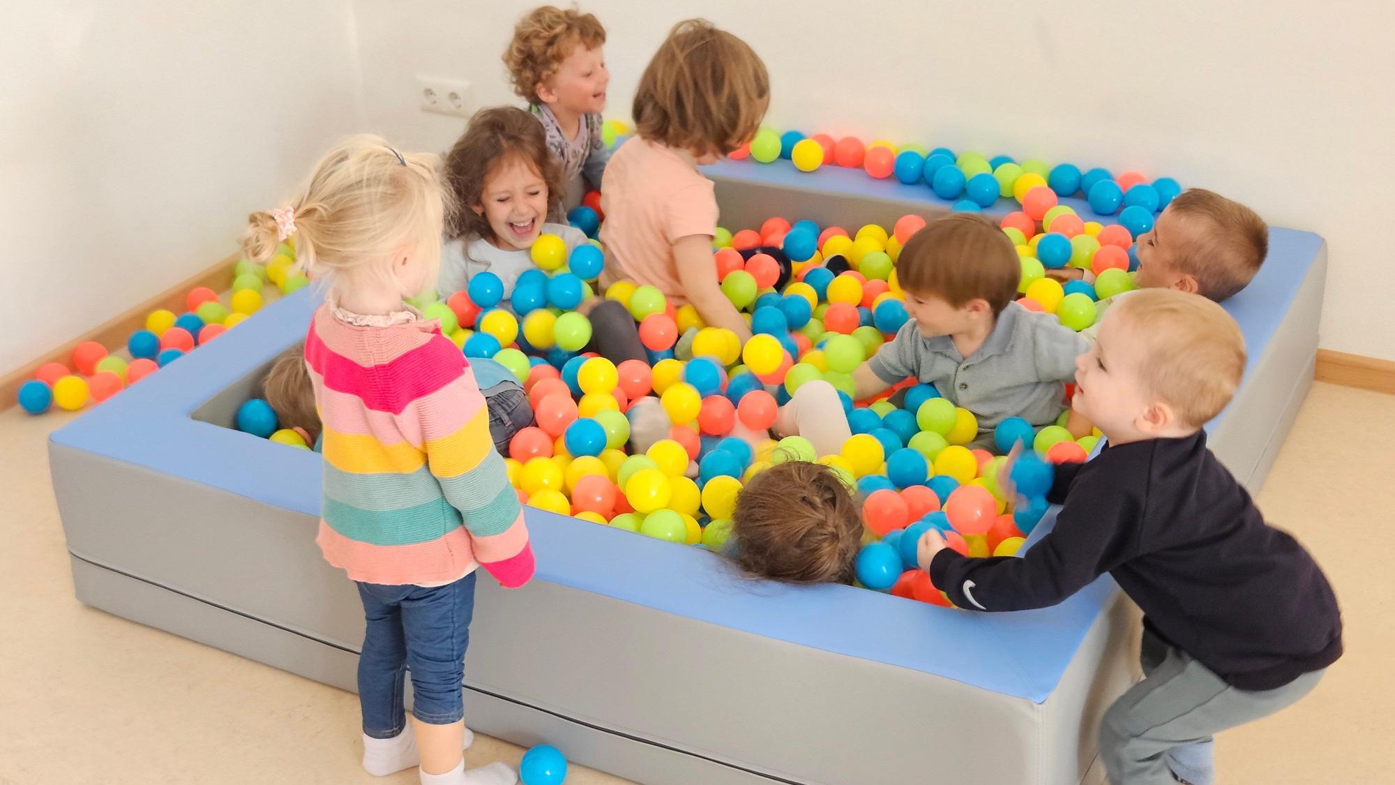 Mehrere Kinder toben in einem Bällebad.