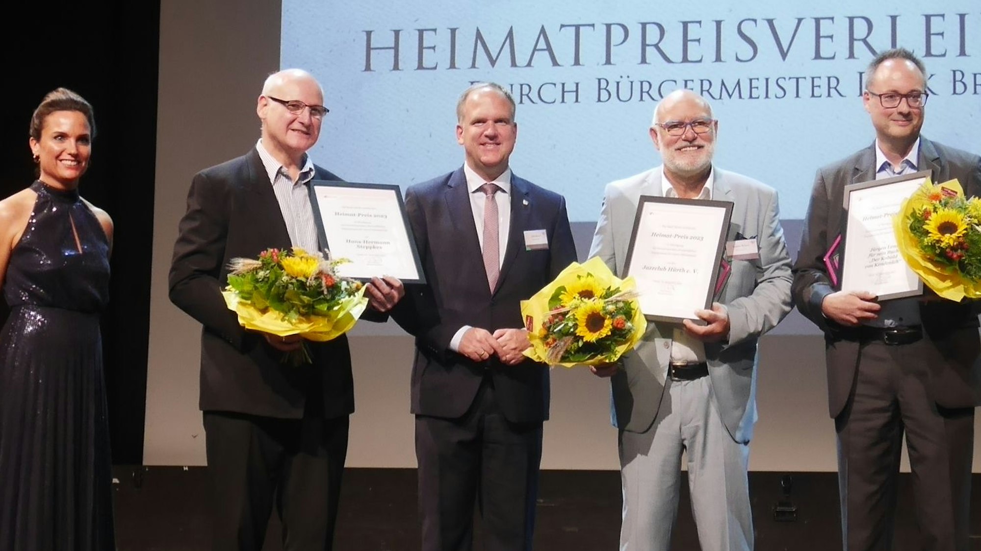 Eine Frau und vier Männer, davon drei mit Urkunden und Blumensträußen.