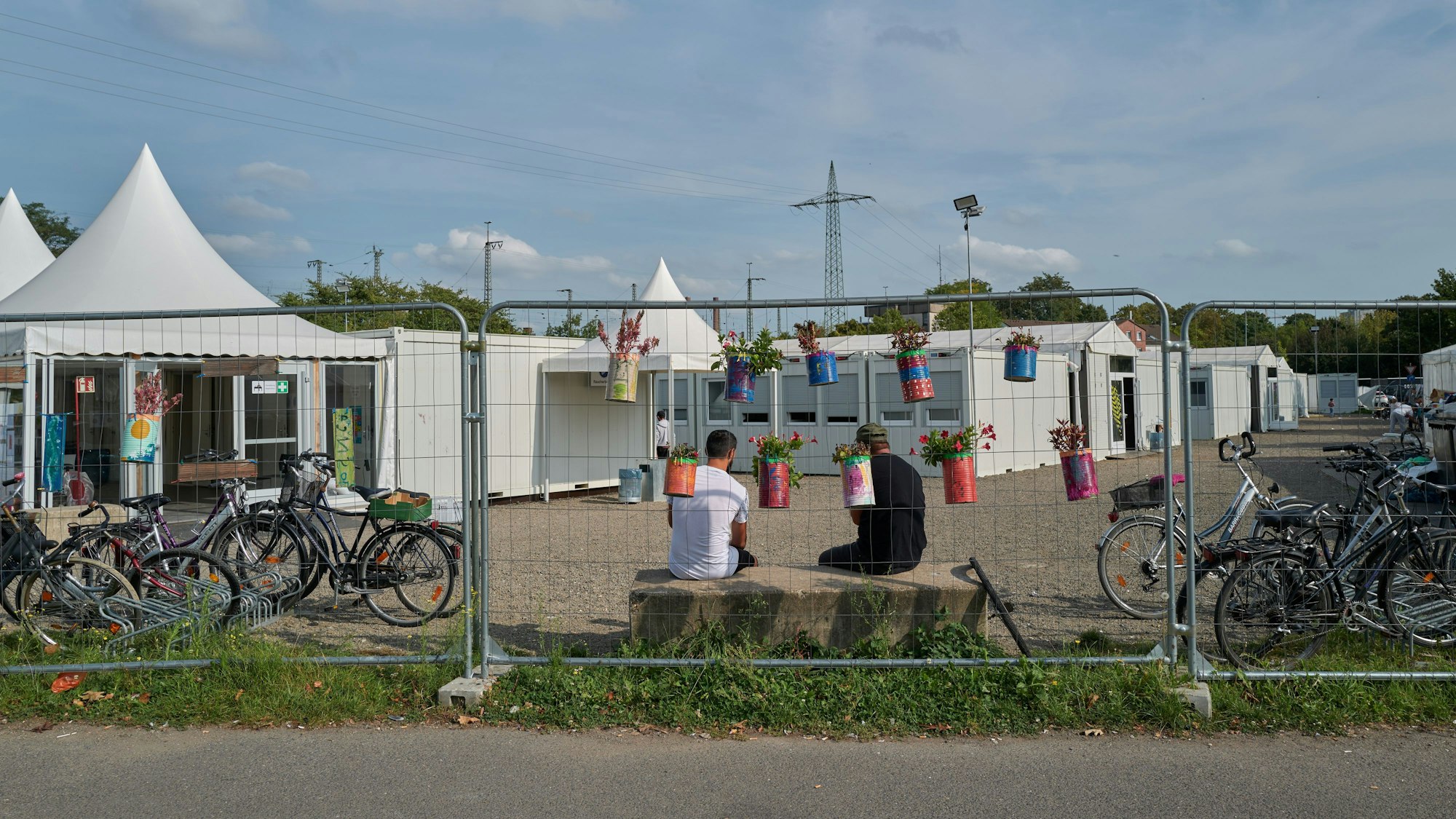 Blick in die Flüchtingsunterkunft am Südstadion: zwei Männer sitzen hinter einem Zaun. Am Zaun hängen Blumentöpfe