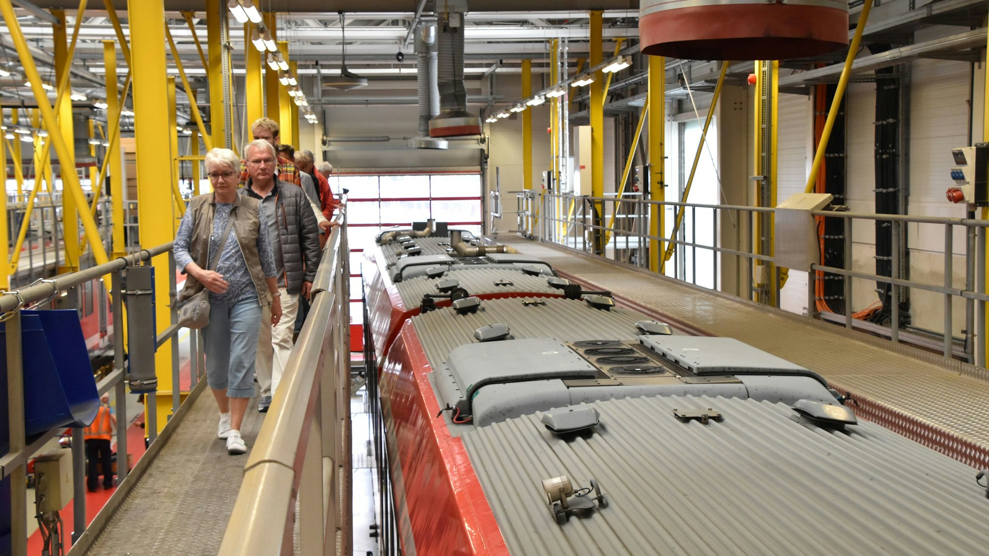 Über einen Gang in luftiger Höhe gehen Menschen in Höhe des Daches am Zug vorbei.