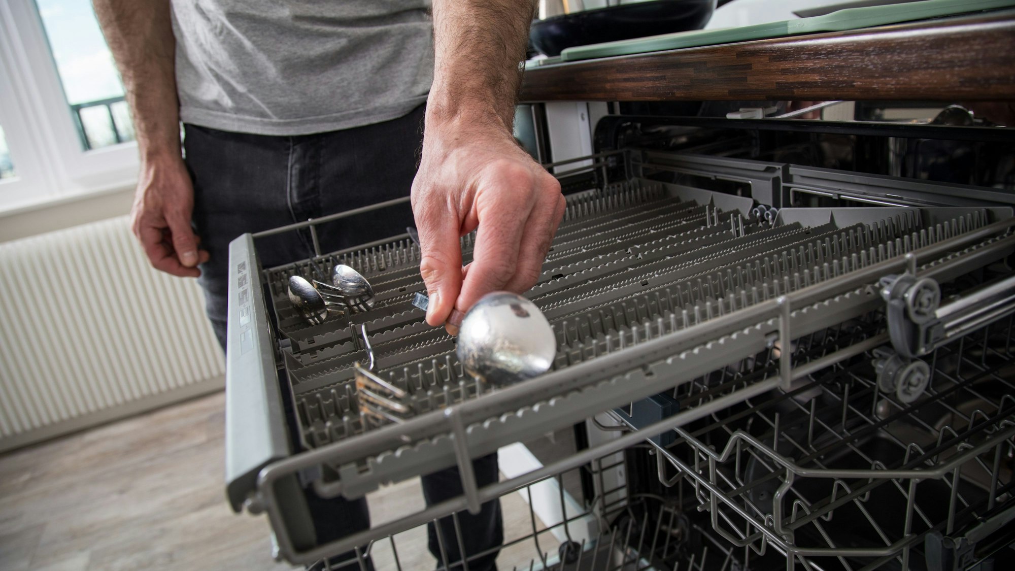Eine Person holt einen Löffel aus der Spülmaschine, auf dem ein rostiger Fleck zu sehen ist