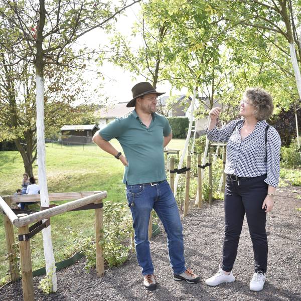 Ein Mann und eine Frau, Christoph Zimmermann und Anne Horst, stehen unter einer Reihe junger Bäume und unterhalten sich.