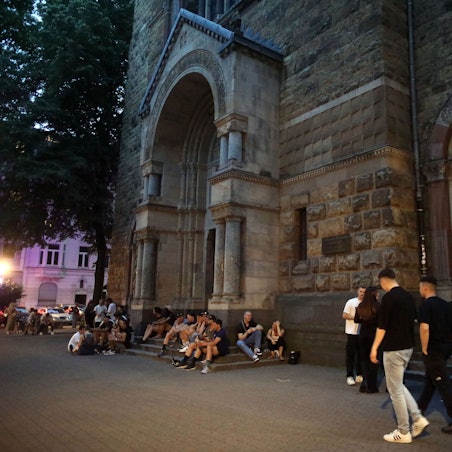Menschen sitzen rund um die Kirche Sankt Michael am Brüsseler Platz.