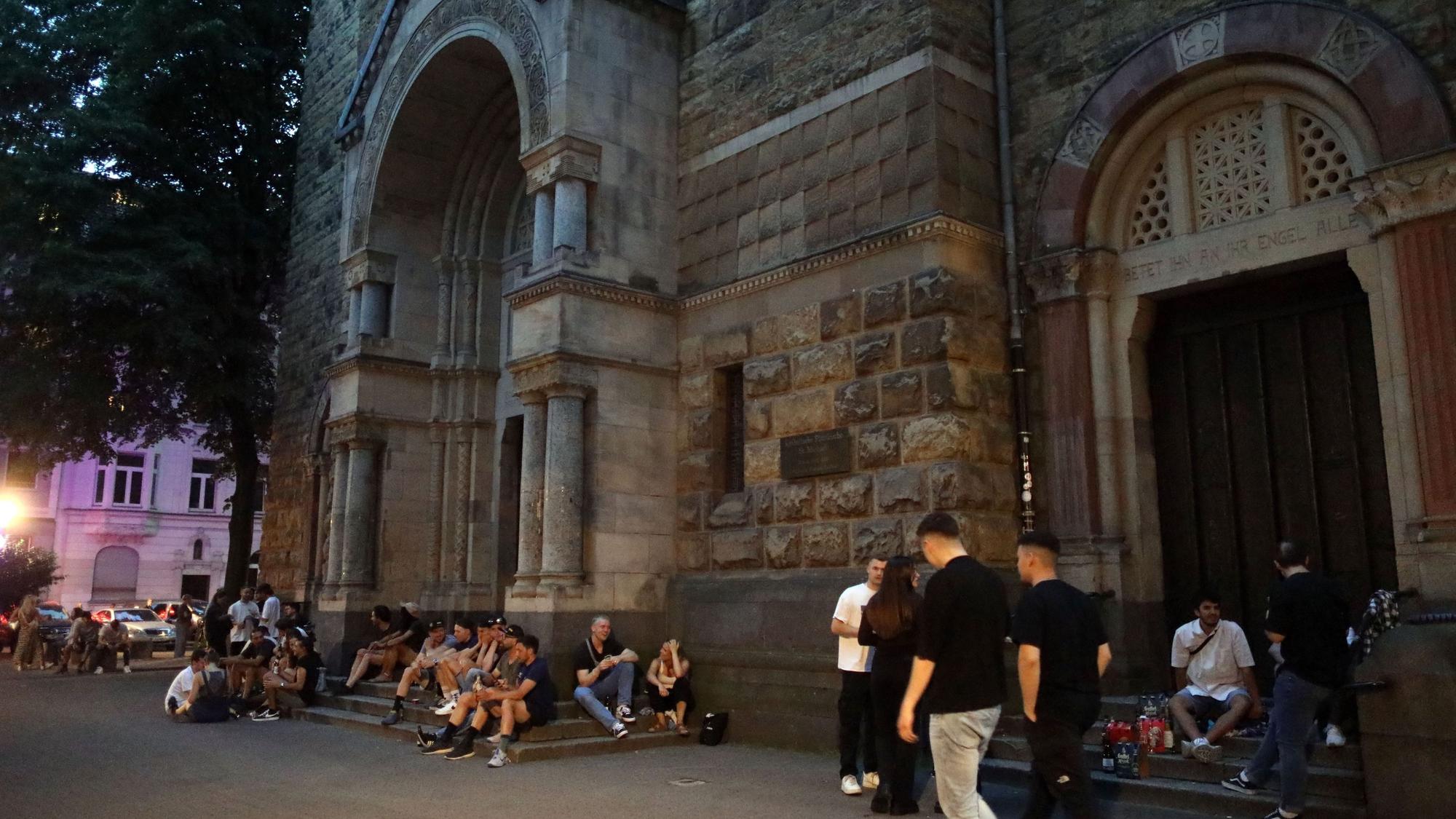 Menschen sitzen rund um die Kirche Sankt Michael am Brüsseler Platz.