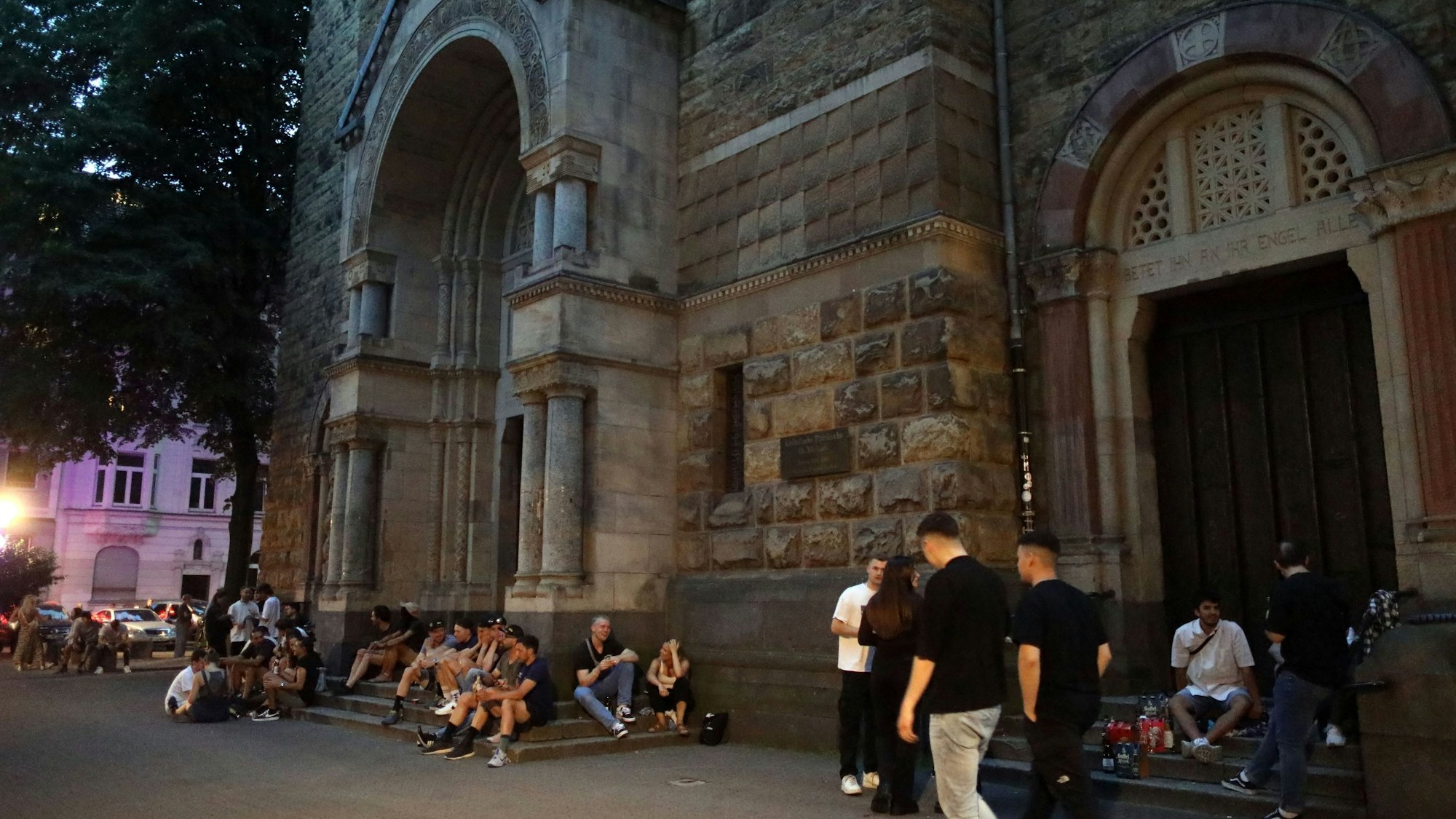 Menschen sitzen rund um die Kirche Sankt Michael am Brüsseler Platz.